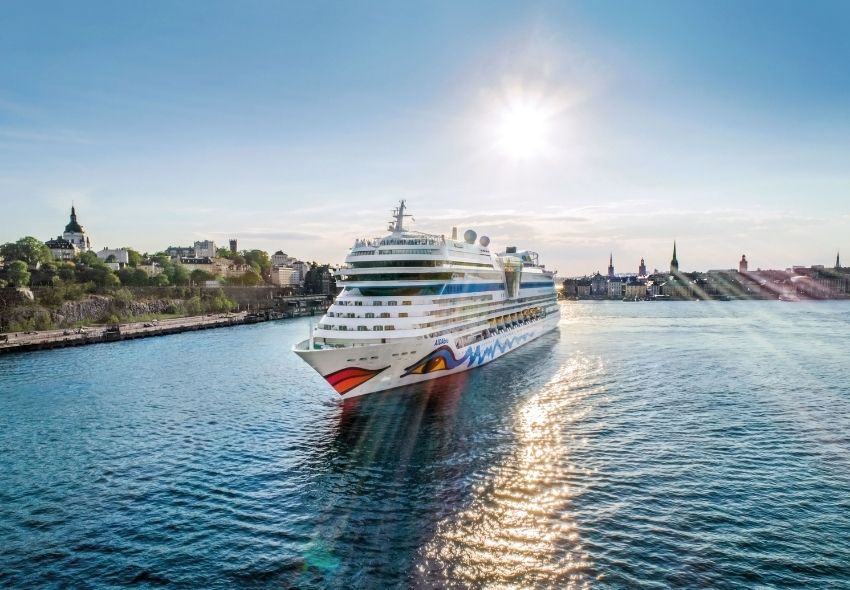 AIDAmar im Hafen von Stockholm AIDAmar fährt bei sonnigem Wetter auf dem Wasser vor der Skyline von Stockholm. Das Kreuzfahrtschiff liegt vor der Stadtkulisse mit historischen Gebäuden und Kirchtürmen.