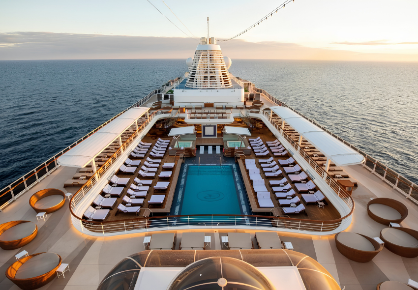 Pooldeck der Seven Seas Prestige Blick von oben auf das offene Pooldeck der Seven Seas Prestige mit zentralem Pool, zahlreichen Liegen und Sitzbereichen. Im Hintergrund ist das offene Meer bei Sonnenuntergang zu sehen.