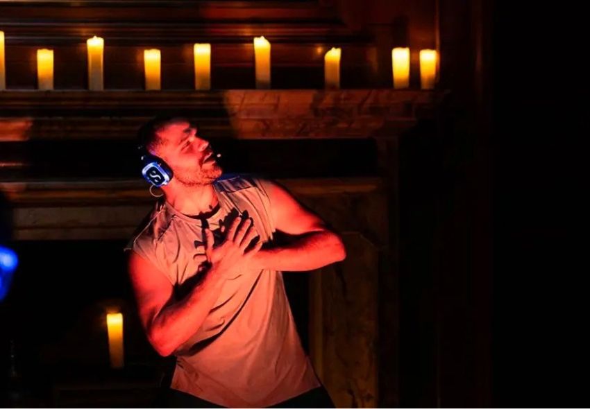 Sanctum-Wellnesskonzept Eine Person mit Kopfhörern führt eine Bewegungsübung in stimmungsvoll beleuchteter Umgebung mit Kerzenlicht aus. Das Bild zeigt das neue Sanctum-Konzept, das Bewegung, Musik und Achtsamkeit verbindet.
