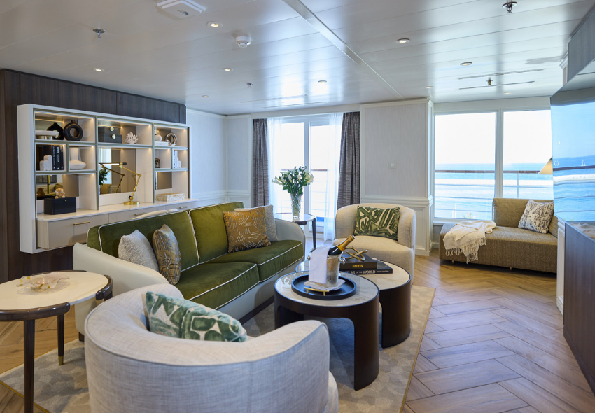Wohnbereich einer Suite der Seven Seas Voyager Eine modern eingerichtete Suite der Seven Seas Voyager mit Sitzbereich, Sofa und bodentiefen Fenstern zum Balkon. Die Innenausstattung kombiniert helle Töne mit Holzdetails und maritimen Akzenten.