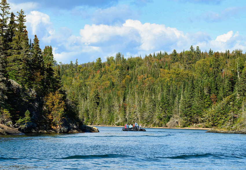 Landschaftsbild aus Kanada Ein Schlauchboot mit Menschen darin schwimmt auf einem blauen Fluss vor einem grünen Waldgebiet