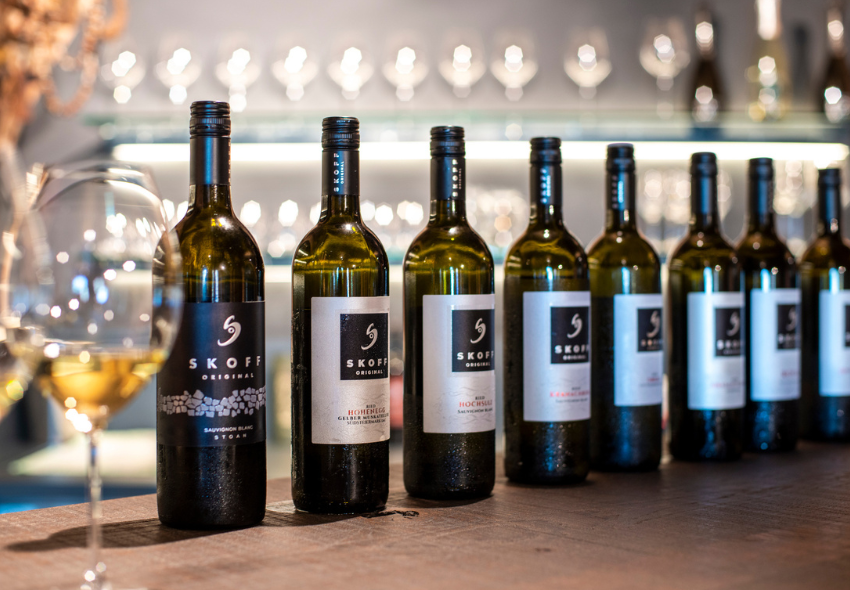 Wein & Kultur auf Mein Schiff Acht Weinflaschen vom Weingut Skoff auf dem Tisch nebeneinander, links davon ein Weinglas mit Weißwein