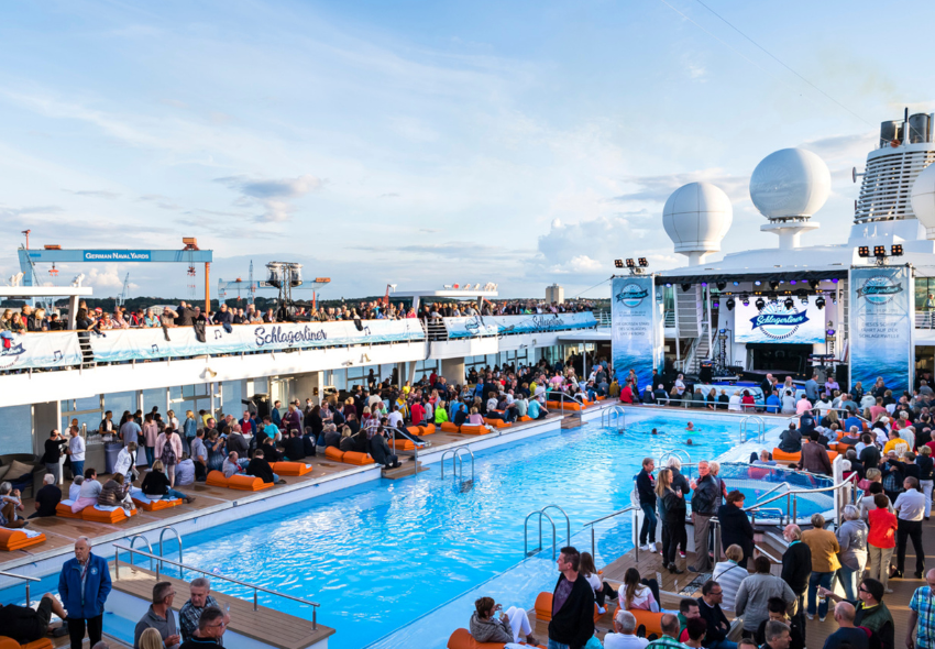Poolbereich auf Mein Schiff, mit Menschen drum herum und Schlagerliner Bühne
