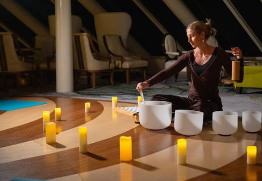 Wellness at Sea-Retreats 2027 Frau macht Yoga auf dem Boden mit Kerzen, im Hintergrund Fenster und Stühle