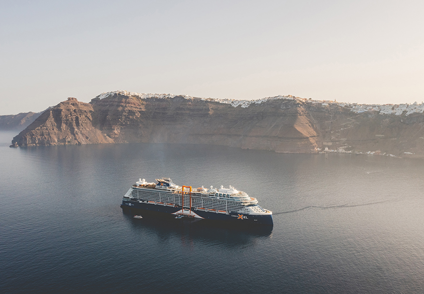 Celebrity Xcel auf dem Meer vor Küste von Santorini mit weißen Gebäuden