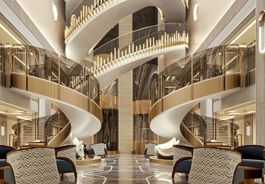 Das helle, mehrstöckige Starlight Atrium der Seven Seas Prestige mit geschwungenen weißen Treppen, goldfarbenen Geländern und zahlreichen leuchtenden Kristallstäben entlang der Treppen. Im Vordergrund befinden sich mehrere Sitzgruppen.