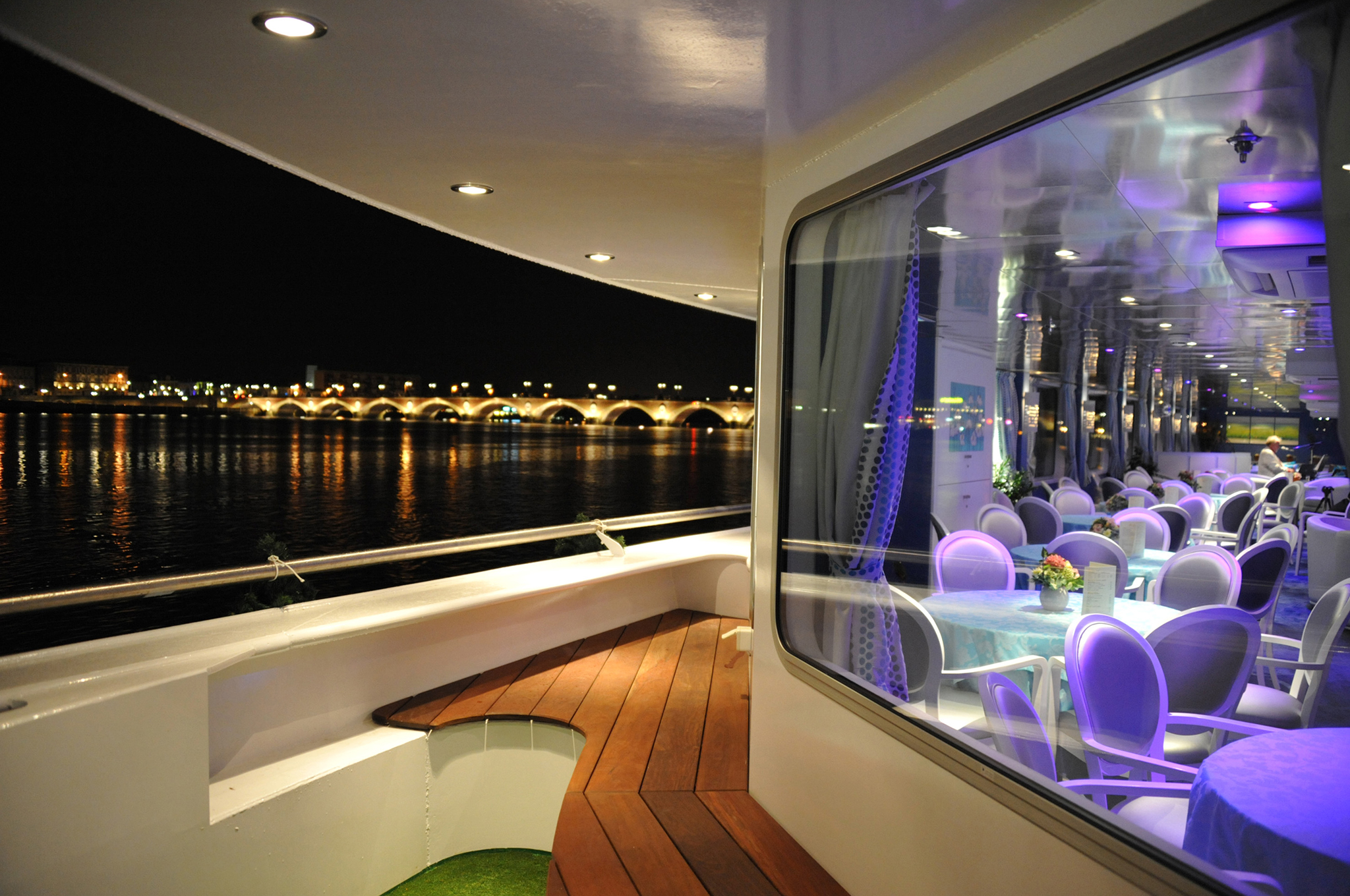 Außenbereich der Lounge Bar auf der MS CYRANO DE BERGERAC bei Nacht mit großen Panoramafenstern und Blick auf eine beleuchtete Brücke