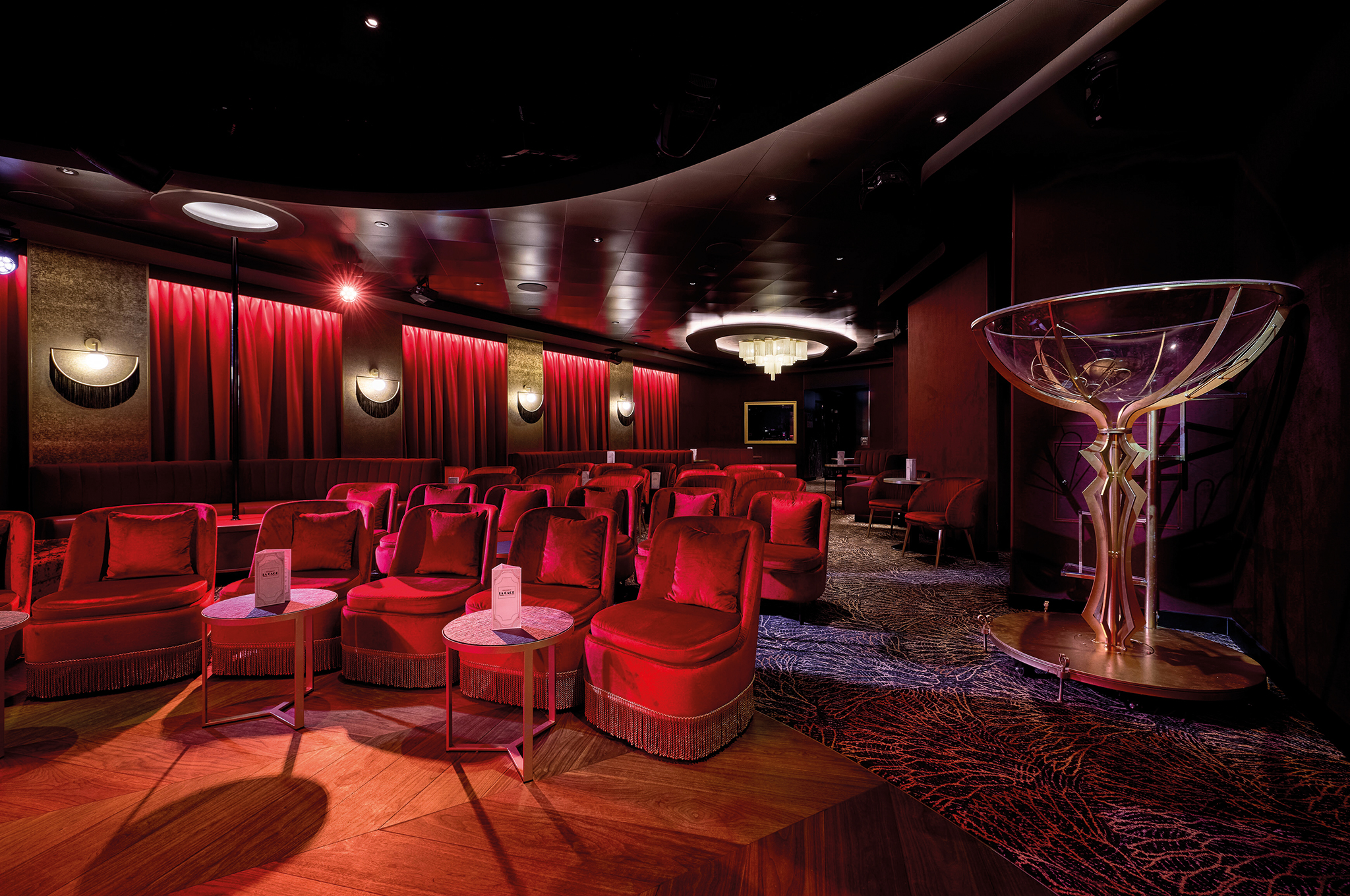 Interior view of La Cage- Casino&Bar&Burlesque on Mein Schiff Flow with plush seating and a large cocktail glass sculpture.