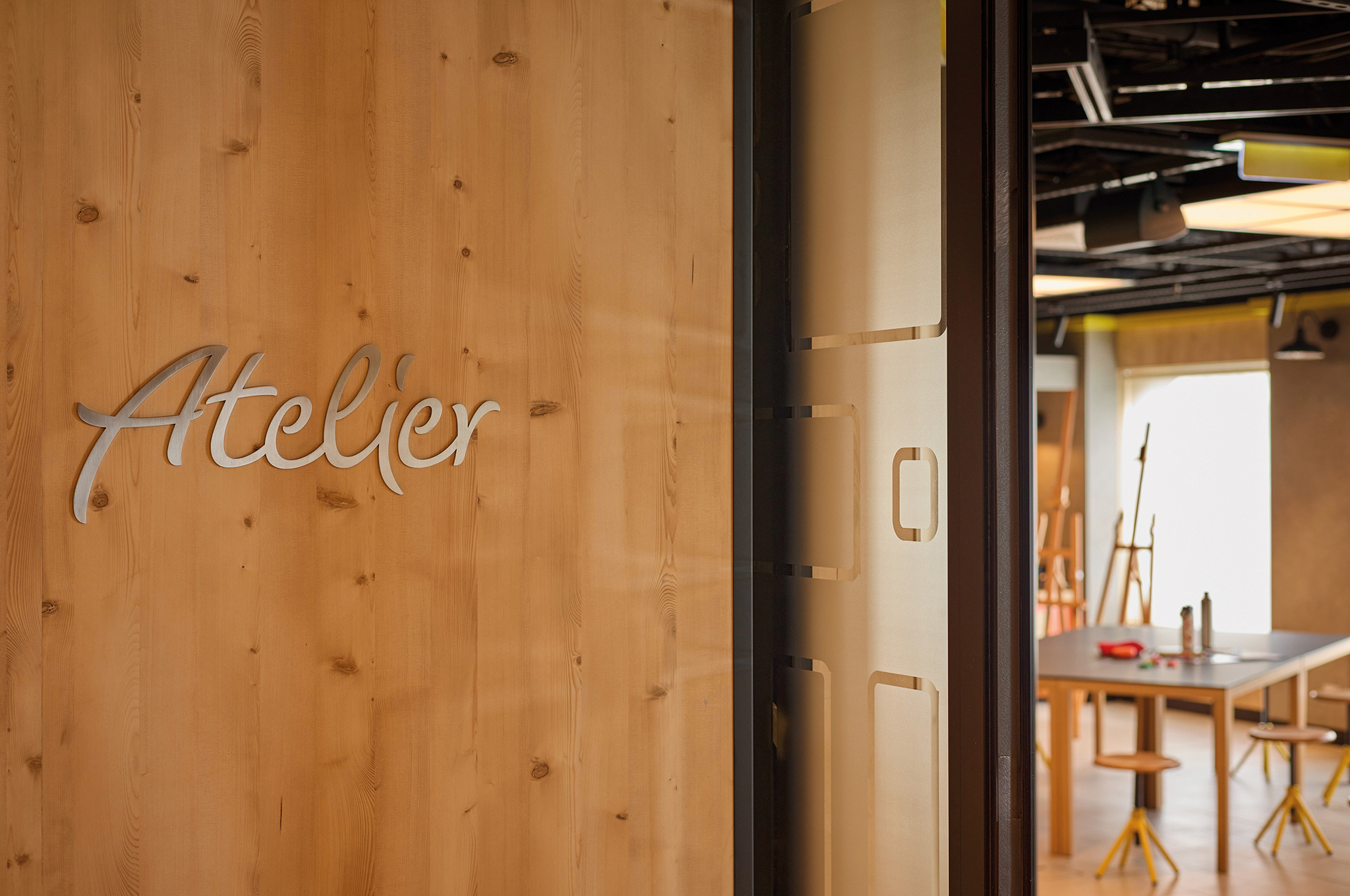 Holztafel mit der Beschriftung Atelier und Blick in den Kreativraum der Mein Schiff Flow