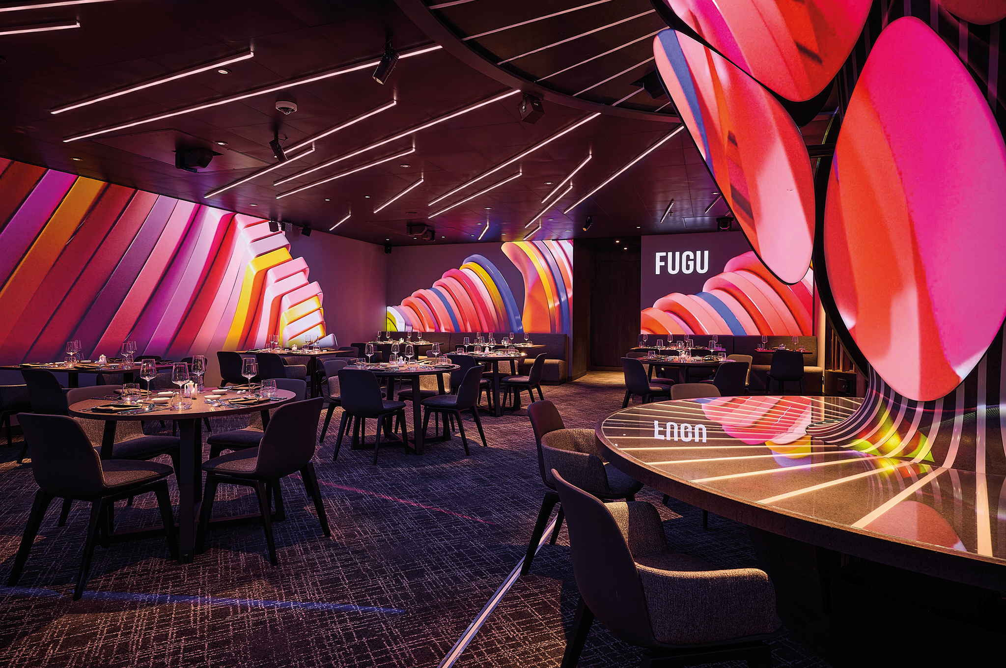 Innenansicht des japanischen Restaurants Fugu an Bord der Mein Schiff Flow mit modernen Tischen und leuchtenden Wanddekorationen.